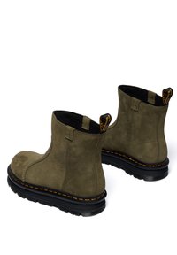 Botines de ante verde oliva con suela de goma negra, costuras amarillas y tiradores. Presentan una textura suave y un diseño sencillo.