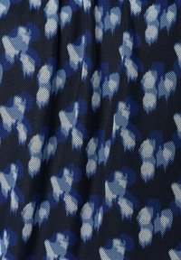 Blau- und Weiß abstraktes florales Muster auf einem strukturierten marineblauen Stoff, mit einem netzartigen Design und unterschiedlichen Formen und Größen von Blumen.