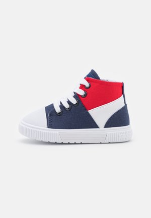 Zapatilla alta para niños con suela blanca, puntera blanca, cordones blancos y paneles de tela en azul marino, rojo y blanco.