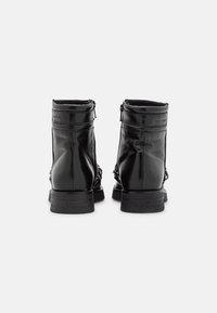 Par de botas de cuero negro hasta el tobillo con suelas de textura gomosa, vistas desde atrás sobre un fondo blanco plano.