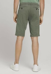 Shorts vert olive avec une texture subtile, dotés de deux poches arrière avec boutons, ourlets retroussés, portés avec des baskets blanches.