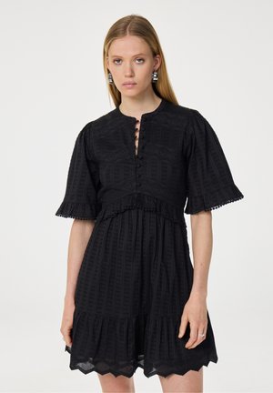 Zwarte jurk met korte pofmouwen, knoopsluiting bij de hals en een tiered ruffle zoom. Heeft een gestructureerde stof met geometrische patronen en kantaccenten.