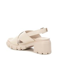 Sandalias abiertas de punta beige con un diseño de correas cruzadas, correa trasera ajustable, tacón grueso y texturizado, y material suave similar al cuero.