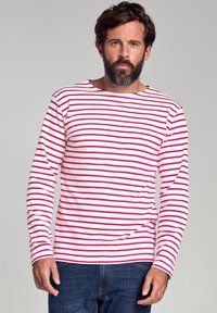 Langærmet stribet skjorte i hvid med røde horisontale striber, lavet af et blødt stof. Båret med blå jeans og med en båd-udskæring.