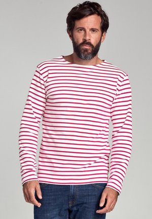 Langærmet stribet skjorte i hvid med røde horisontale striber, lavet af et blødt stof. Båret med blå jeans og med en båd-udskæring.