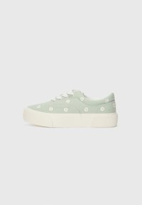 Green canvas sneaker with white daisy embroidery, white laces, and a thick white rubber sole. Rounded toe and textured sole for grip.