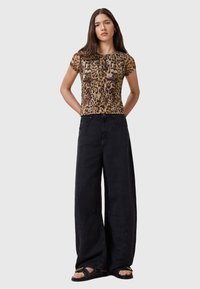Top corto a maniche corte con stampa leopardata, abbinato a pantaloni neri a gamba larga oversize e sandali neri piatti. Tessuto morbido con una texture liscia.