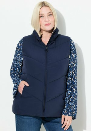 Chaleco acolchado navy con un cuello alto, presenta un acolchado en forma de chevron, cierres frontales y bolsillos laterales, combinado con una blusa de manga larga con un estampado.
