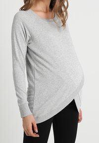 Haut gris à manches longues avec une coupe décontractée, présentant un design croisé à l'avant, des poignets côtelés et un tissu doux et extensible.