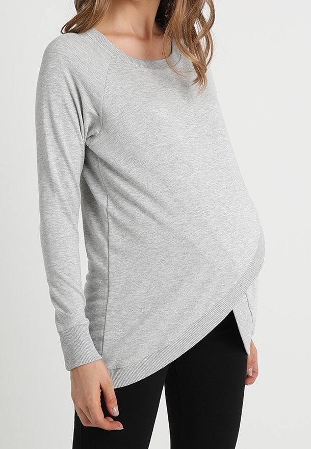 Haut gris à manches longues avec une coupe décontractée, présentant un design croisé à l'avant, des poignets côtelés et un tissu doux et extensible.