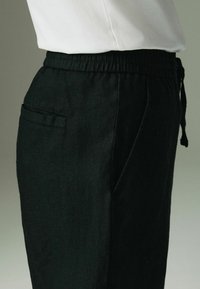 Pantaloni jogger negri din in, cu talie elastică, snur și buzunar lateral, având un finisaj texturat și o croială lejeră.