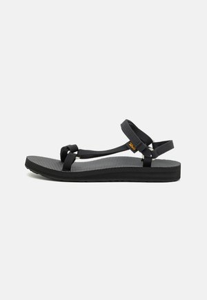 Schwarze Sandalen mit einer strukturierten Sohle, ausgestattet mit verstellbaren Textilriemen und flachem Design. Die Fußbett hat eine leichte Wölbung für zusätzlichen Komfort.