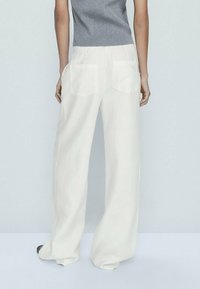 Pantalons larges blancs avec une texture lisse, dotés de deux poches arrière rectangulaires. Associés à un débardeur gris en mailles côtelées.