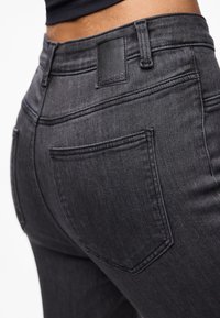 Σκούρο γκρι τζιν παντελόνι με εφαρμοστή σχεδίαση, πίσω τσέπες και μαύρη δερμάτινη ετικέτα στη ζώνη με ανάγλυφο λογότυπο.