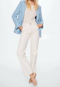 Světle modrý texturovaný blazer přes krémový přiléhavý top, doplněný o krémové kalhoty s vysokým pasem a širokým střihem, a béžové sandály na řemínky.