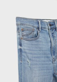 Denim jeans in light blue with a slightly distressed texture. Features front pockets, typical stitching, and a button closure.