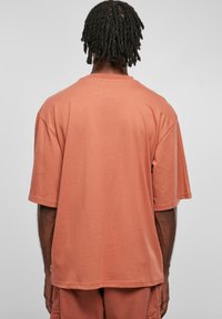 Tricou oversized în culoarea roz prăfuit, fabricat dintr-un material de bumbac moale. Are mâneci scurte și un decolteu rotund, cu o croială lejeră.