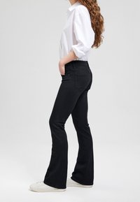 Musta leveälahkeinen farkut, joissa on korkea vyötärö ja etutaskut. Yhdistetty valkoisen napillisen paidan ja valkoisten tennareiden kanssa.