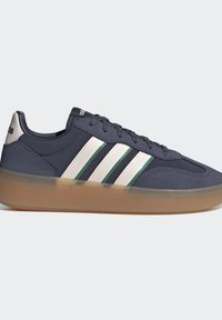 Zapatilla deportiva de caña baja azul oscuro con rayas blancas y verdes, suela marrón translúcida y cierre con cordones, vista lateral sobre fondo claro.