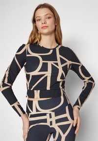 Langermet topp i svart med et beige abstrakt mønster. Laget av elastisk stoff, med en tettsittende fasong og rund halsutringning.