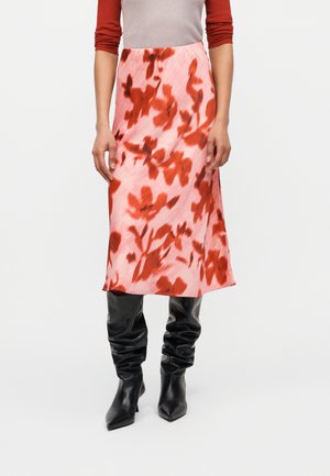 Frau trägt einen knielangen rosa Rock mit rotem Blumenmuster, kombiniert mit schwarzen lässigen kniehohen Stiefeln und einem roten Dreiviertelarm-Top.