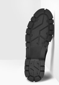 Suela de zapato de goma negra con surcos profundos y patrones texturizados, que presenta un diseño lineal prominente y bordes gruesos y elevados.