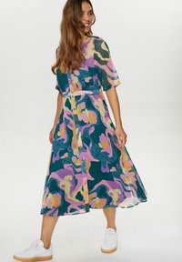 Rochie colorată, cu motive, cu mâneci scurte, având un decolteu cu nasturi, talie ajustată și o fustă lungă până la gleznă. Pur și simplu cu teniși albi.