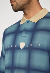 Πολό φανέλα γκολφ Nike σε τυρκουάζ με μπεζ γιακά και υφασμάτινο σχέδιο. Διαθέτει λογότυπο και κουμπωτή λαιμόκοψη.