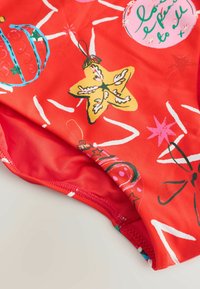 Czerwony materiał kostiumu kąpielowego z zabawnym nadrukiem ornamentów, gwiazdek i zawijasów w zielonym, różowym i żółtym kolorze, o gładkiej fakturze i obszytych brzegach.