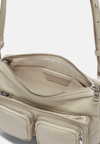 Beżowa skórzana torebka na ramię z wieloma kieszeniami zapinanymi na zamek, wewnętrzna podszewka z jasnego materiału oraz akcenty w srebrnym kolorze.