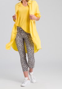 Chemise jaune à boutons portée par-dessus un T-shirt jaune, accompagnée d'un pantalon imprimé léopard à mi-mollet et de baskets blanches.