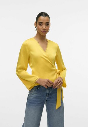 Blouse jaune enroulée avec de longues manches évasées, dotée d'une dentelle le long de l'encolure et des manches. Tissu doux et lisse avec un détail de taille nouée.