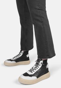 Baskets montantes noir et blanc avec une semelle en caoutchouc texturé, lacets gris et des détails de couture proéminents. Assorties avec un jean foncé.