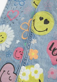 Tissu en denim avec des motifs imprimés colorés comprenant des visages souriants, des cœurs, des marguerites et diverses fleurs en rose, orange, vert, bleu et jaune.