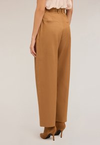 Hoge taille, wijde broek van warm tan materiaal. Bevat netjes vervaardigde zakken en een bijpassende riem. Gladde textuur met strakke lijnen.