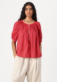 Red short-sleeve blouse with gathered neckline, featuring a grid pattern in blue tones and a button-down front. Soft, lightweight fabric.