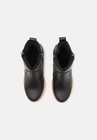 Bottines noires en cuir avec une texture lisse, bout rond, doublure en fausse fourrure et zips sur le côté. Présente une semelle extérieure marron clair avec du fil. 