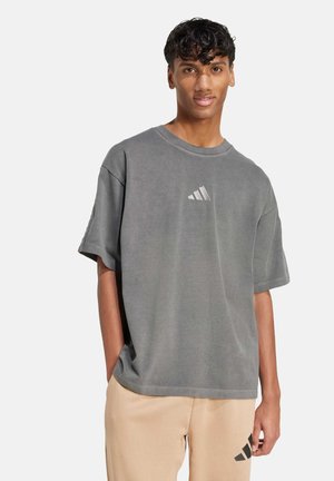 Grå oversized t-shirt i mjukt tyg, med en tryckt tre-stripes-logotyp på bröstet och en avslappnad passform. Idealisk för vardagsbruk.