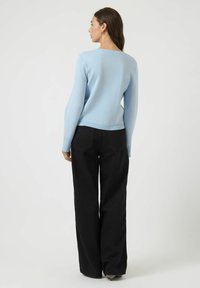 Lys blå ribbestrikket genser med rund hals, kombinert med løstsittende svarte jeans. Har lange ermer og rett kant.