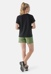 Maglietta nera a maniche corte abbinata a pantaloni corti verdi. La maglietta ha un design semplice; i pantaloni corti sono leggeri, dotati di tasche e con finitura opaca.