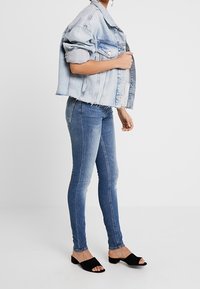 Světle modrá roztrhaná džínová bunda s ohrnutými rukávy, zkombinovaná s těsnými tmavě modrými džíny a černými otevřenými sandály.