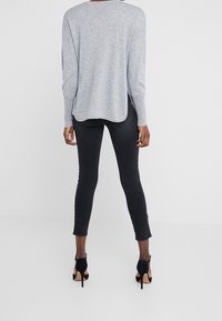 Pull gris à manches longues, texture douce, fentes sur les côtés, associé à un jean skinny noir et des chaussures à talons hauts noires, vu de l'arrière.