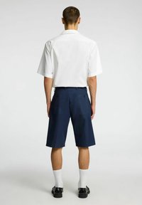 Hvid kortærmet skjorte med krave, parret med knælange marineblå shorts med to baglommer og sorte knapper. Båret med hvide sokker og sko.