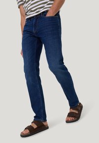 Donkerblauwe denim jeans met een rechte snit, aangevuld met een gestreept, lichtgewicht shirt en bruine sandalen met twee banden.
