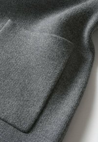 Gros plan sur un tissu en laine gris avec une poche rectangulaire cousue et une surface à texture douce.