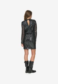 Vestido negro de lentejuelas con silueta ajustada, mangas largas de gasa y detalle en la parte de atrás con forma de ojo de cerradura. Llevado con botas negras hasta la rodilla.