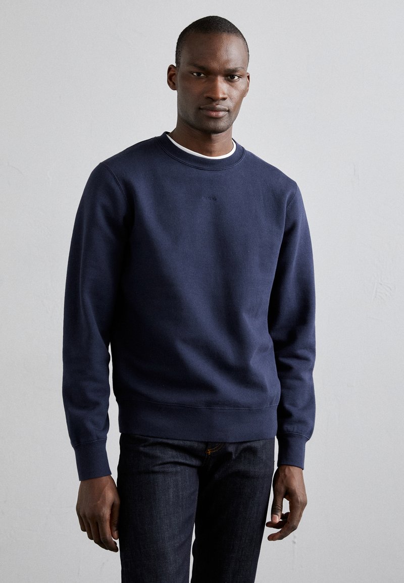 Marineblaue Sweatshirt aus weichem Material mit Rundhalsausschnitt und gerippten Bündchen. Kombiniert mit dunklen Jeans für einen lässigen Look.