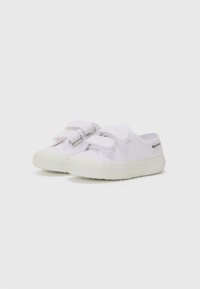 Zapatillas de lona blancas con una suela de goma texturizada. Cuentan con dos correas ajustables de velcro y un diseño elegante y de perfil bajo.