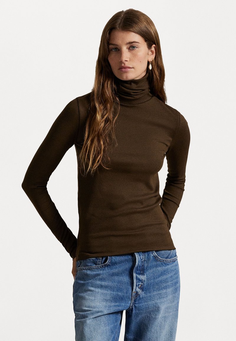 Brauner Rollkragenpullover mit langen Ärmeln in einem figurbetonten Design, aus geripptem Stoff. Kombiniert mit hellblauen Jeans.