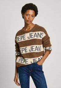 Maglione a righe marroni e crema con il testo "PEPE JEANS", realizzato in materiale morbido, con scollatura rotonda e vestibilità rilassata, abbinato a jeans blu.
